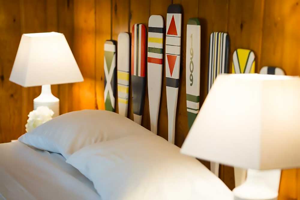 Huron-bedroom-5 A cozy bedroom at South Shore Resort and Retreats features a wooden headboard adorned with colorful, decorative paddles, flanked by two white lamps, ideal for a peaceful retreat in West Michigan.| South Shore Resort & Retreats in West Michigan