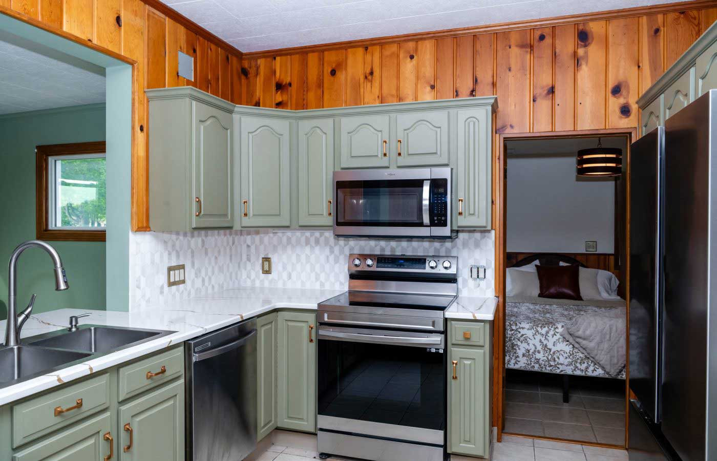 The-lodge-image-10 A cozy kitchen with green cabinets and modern appliances opens to a bedroom at the South Shore Resort and Retreats, offering a peaceful retreat for a Lake Michigan getaway in West Michigan.| South Shore Resort & Retreats in West Michigan