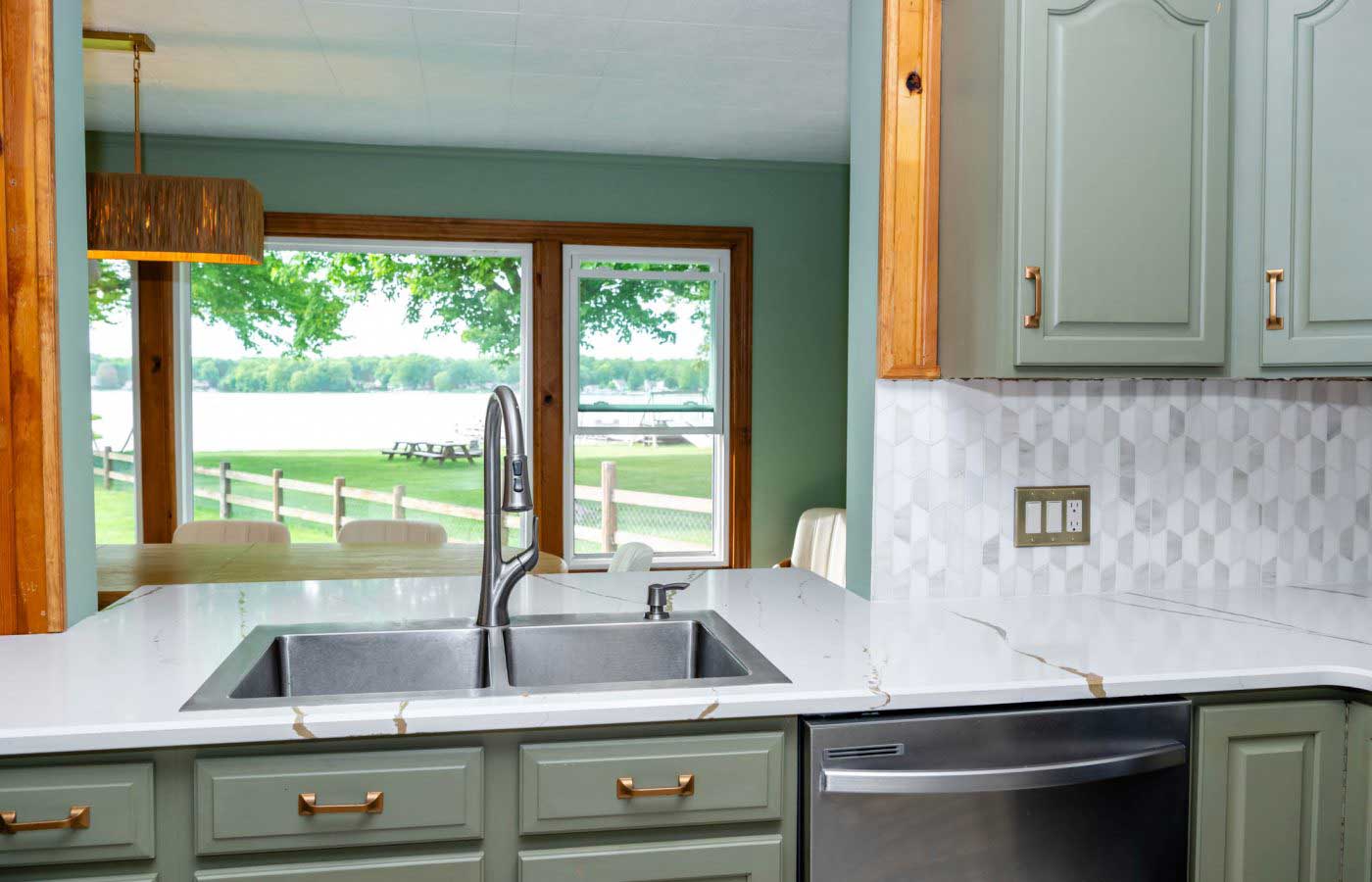 The-lodge-image-11 A modern kitchen with green cabinets and a marble countertop overlooks a serene lake through large windows, offering a peaceful retreat at South Shore Resort and Retreats, ideal for a relaxing getaway in West Michigan.| South Shore Resort & Retreats in West Michigan