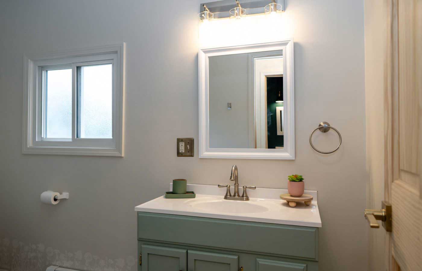 The-lodge-image-8 A serene bathroom at South Shore Resort and Retreats features a light green vanity, round mirror, and potted plant, offering a peaceful retreat ideal for a relaxing getaway in West Michigan.| South Shore Resort & Retreats in West Michigan
