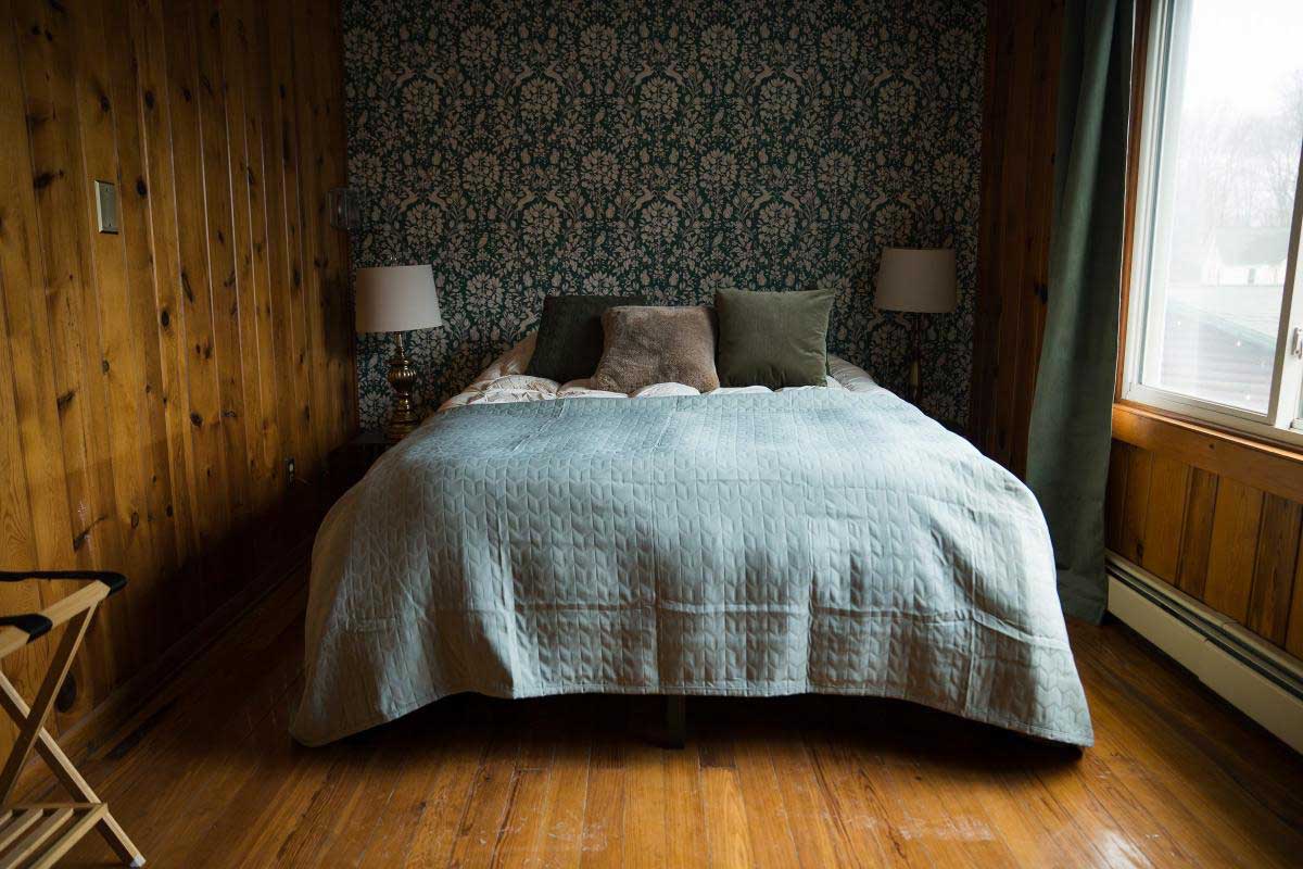 lodge-bedroom-2 A cozy bedroom with wood-paneled walls and a large bed adorned with green and beige pillows, creating a warm, inviting atmosphere at South Shore Resort and Retreats, perfect for a relaxing getaway in West Michigan.| South Shore Resort & Retreats in West Michigan