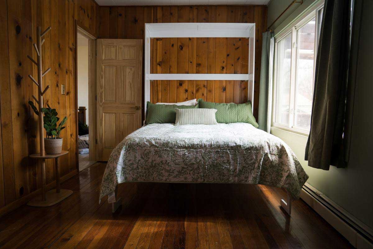 lodge-bedroom-4 A cozy bedroom with wood-paneled walls features a large bed adorned with green and white bedding, offering a peaceful retreat at South Shore Resort and Retreats, ideal for a relaxing getaway.| South Shore Resort & Retreats in West Michigan
