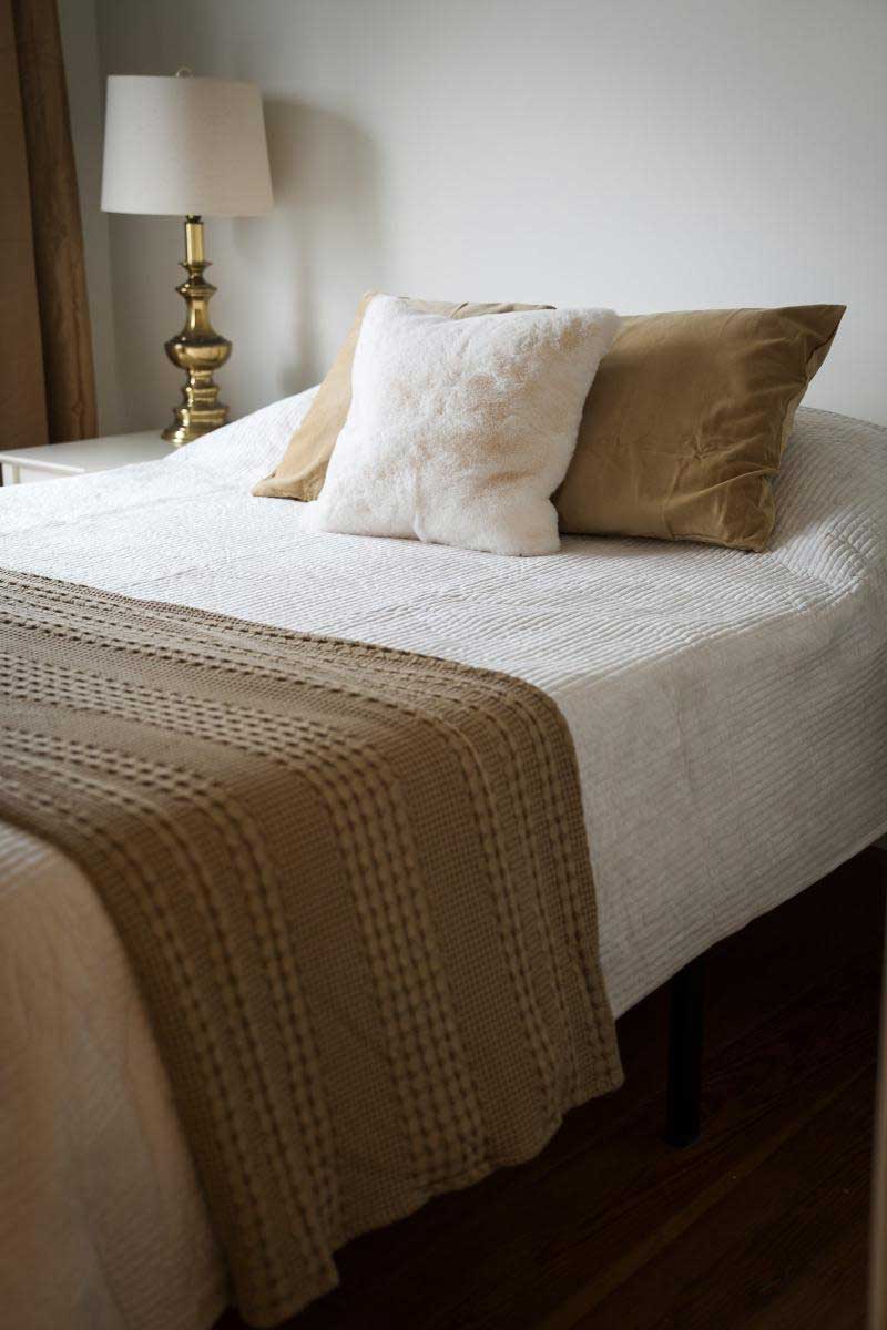 lodge-bedroom-7 Cozy bedroom with white and beige bedding and a gold lamp, ideal for a relaxing getaway at South Shore Resort and Retreats, offering welcoming and peaceful accommodations in West Michigan.| South Shore Resort & Retreats in West Michigan