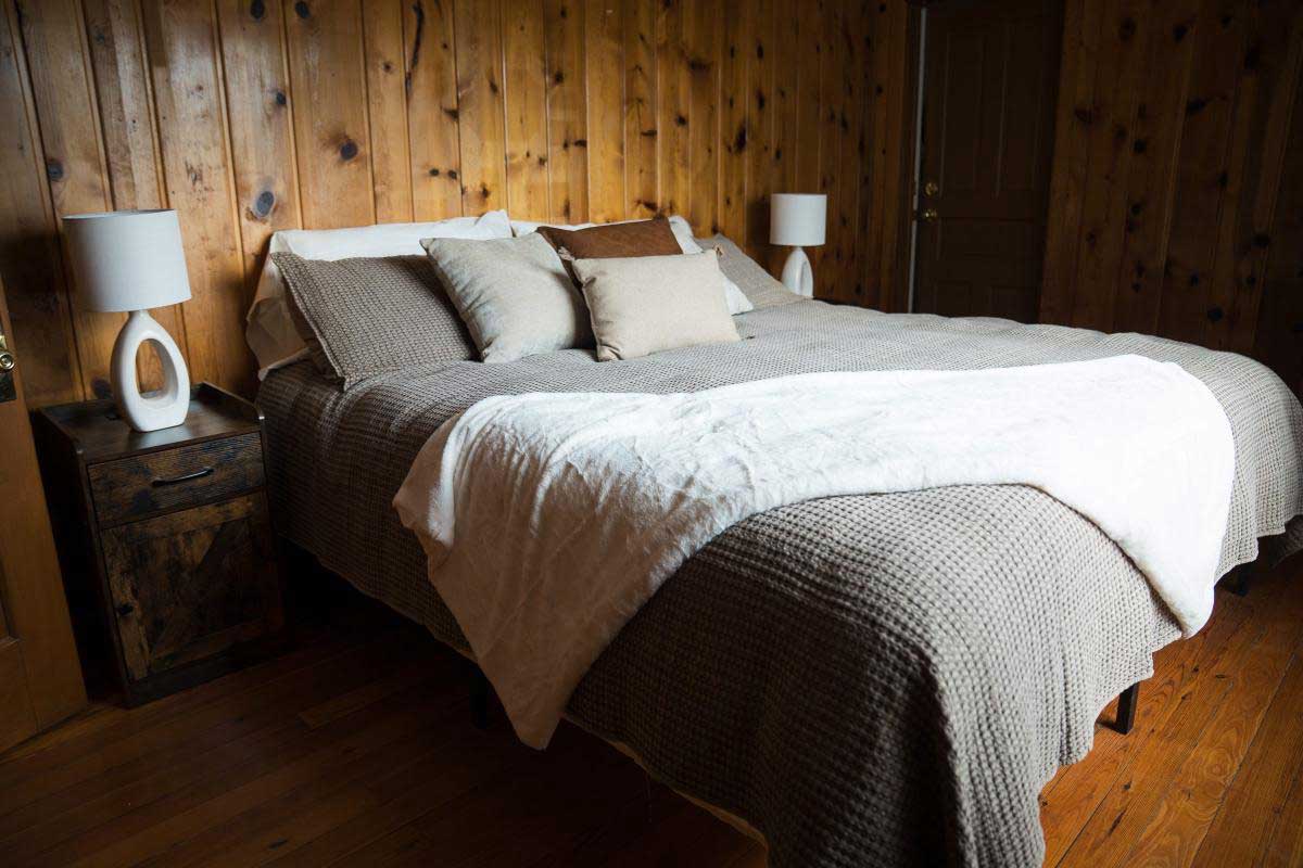 lodge-bedroom-8 A cozy bedroom with wood-paneled walls, a large bed with plush pillows, and soft lighting, offering a relaxing getaway at South Shore Resort and Retreats, ideal for a peaceful retreat near Lake Michigan.| South Shore Resort & Retreats in West Michigan