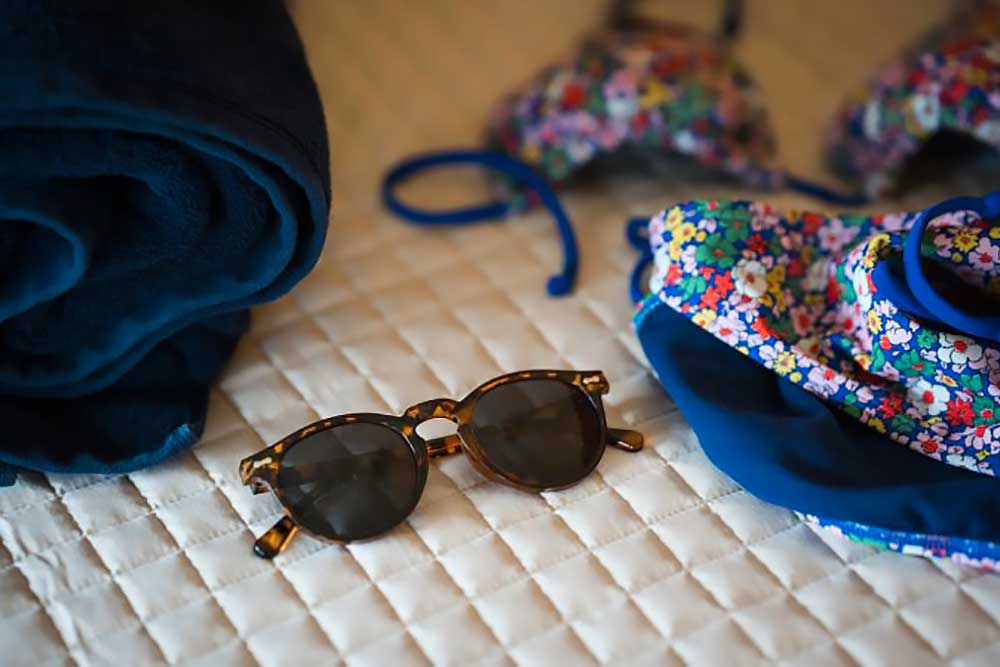 the-huron-image-2 A pair of sunglasses and a colorful floral bikini are laid out on a quilted bedspread, suggesting a relaxing getaway at a lakefront retreat like South Shore Resort and Retreats, ideal for a peaceful retreat in West Michigan.| South Shore Resort & Retreats in West Michigan