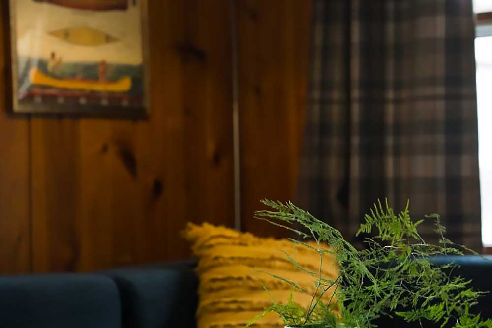 the-huron-image-3 A cozy living room with a blue sofa, yellow cushion, and potted plant creates a welcoming atmosphere at South Shore Resort and Retreats, a perfect spot for a peaceful retreat in West Michigan.| South Shore Resort & Retreats in West Michigan